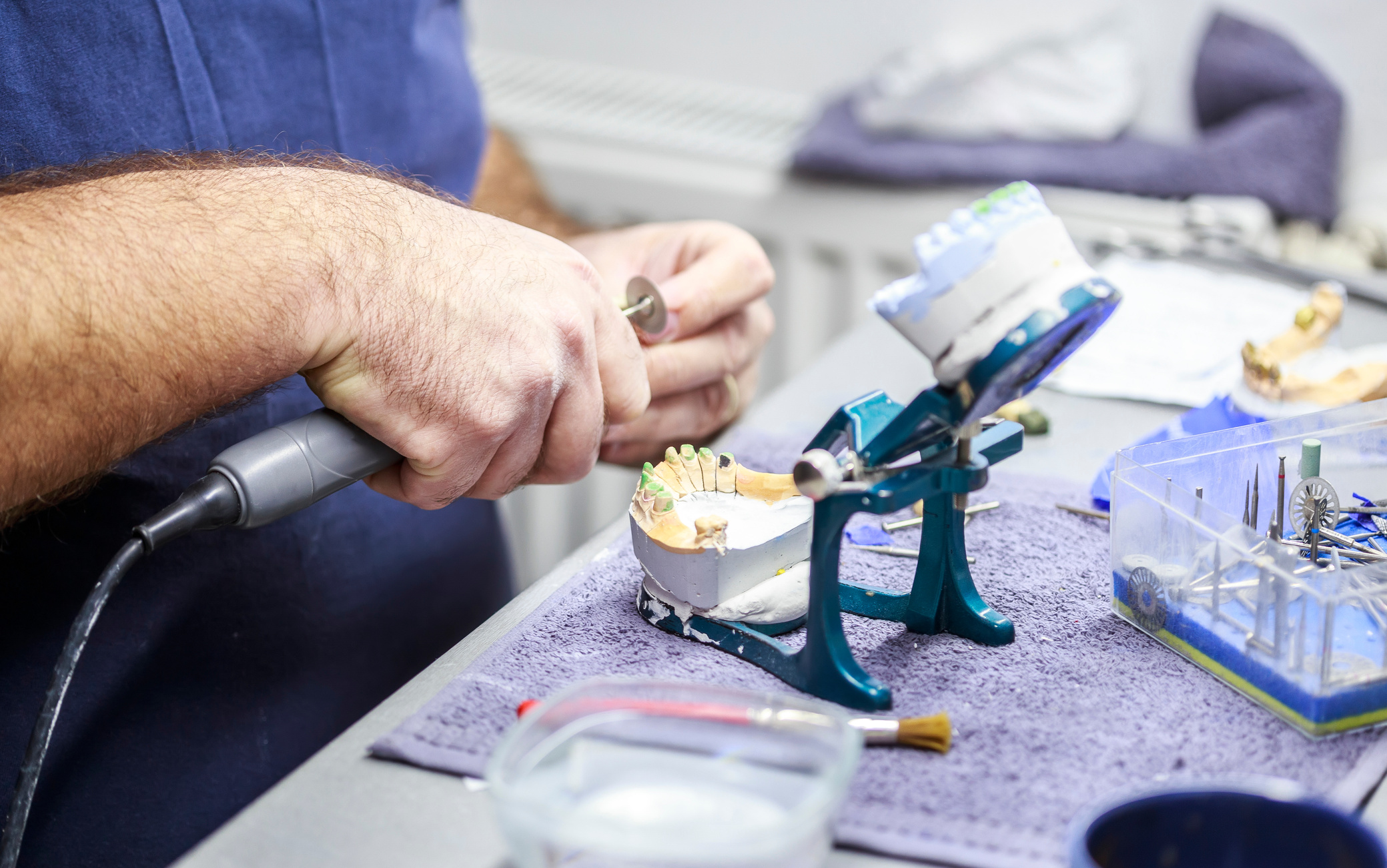 Dental technician working with articulator in dental lab.